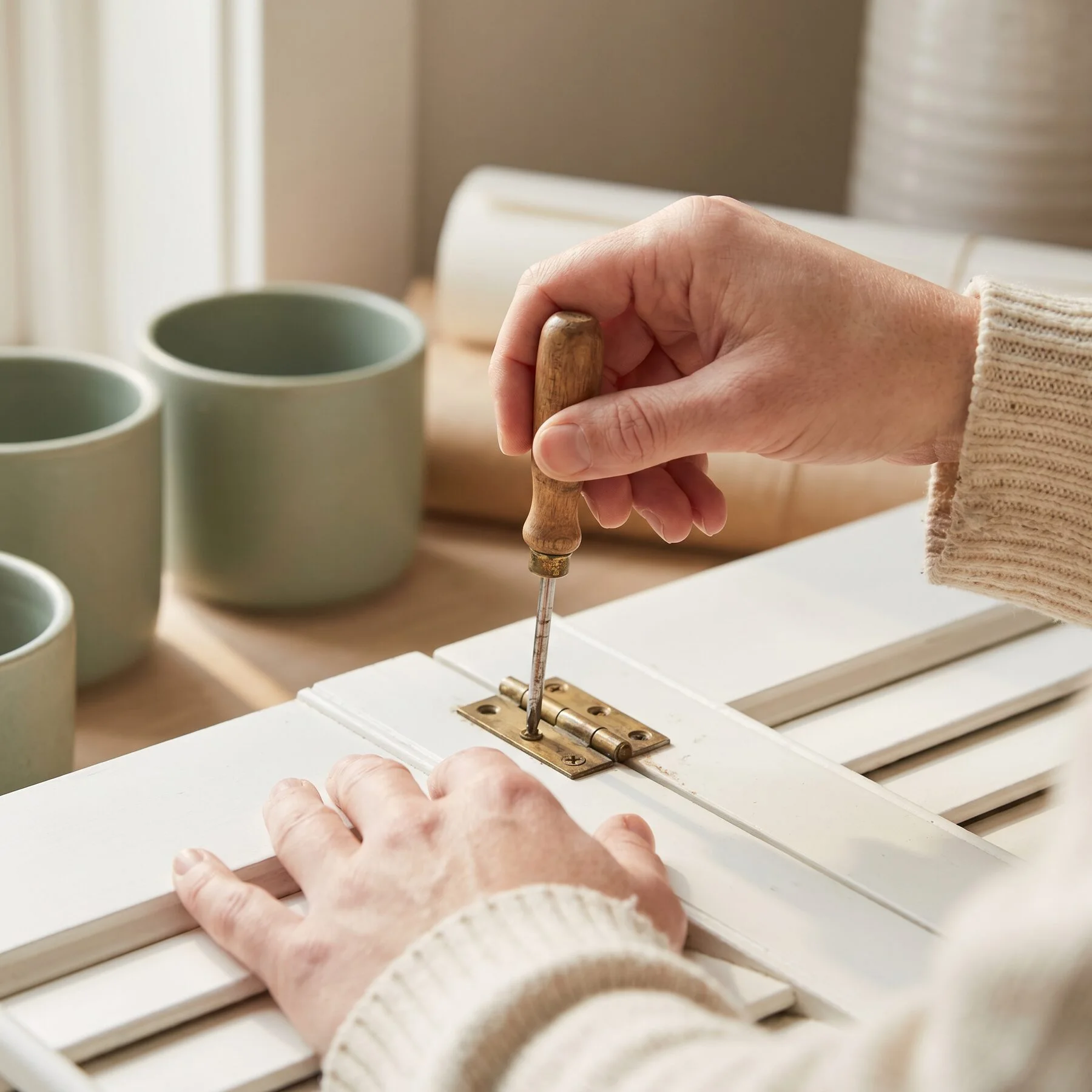 Tightening a brass hinge screw on a shutter panel with a screwdriver
